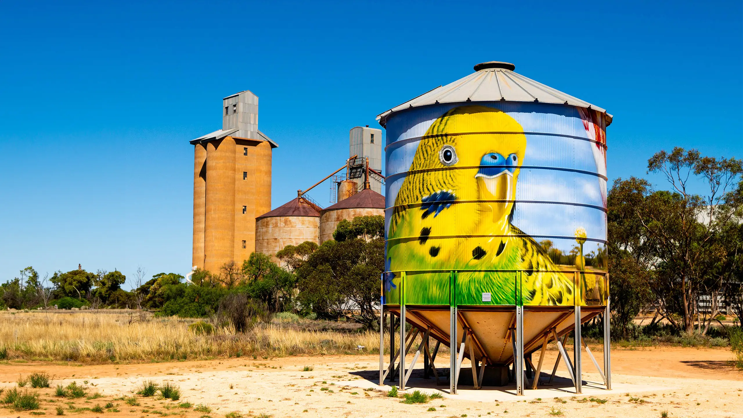 A silo artwork featuring a canary, with a building and more silos in the background.