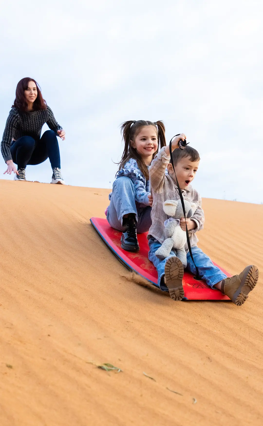 A family enjoying a day out at Perry Sand Hills, with two kids sliding down the sand dunes.